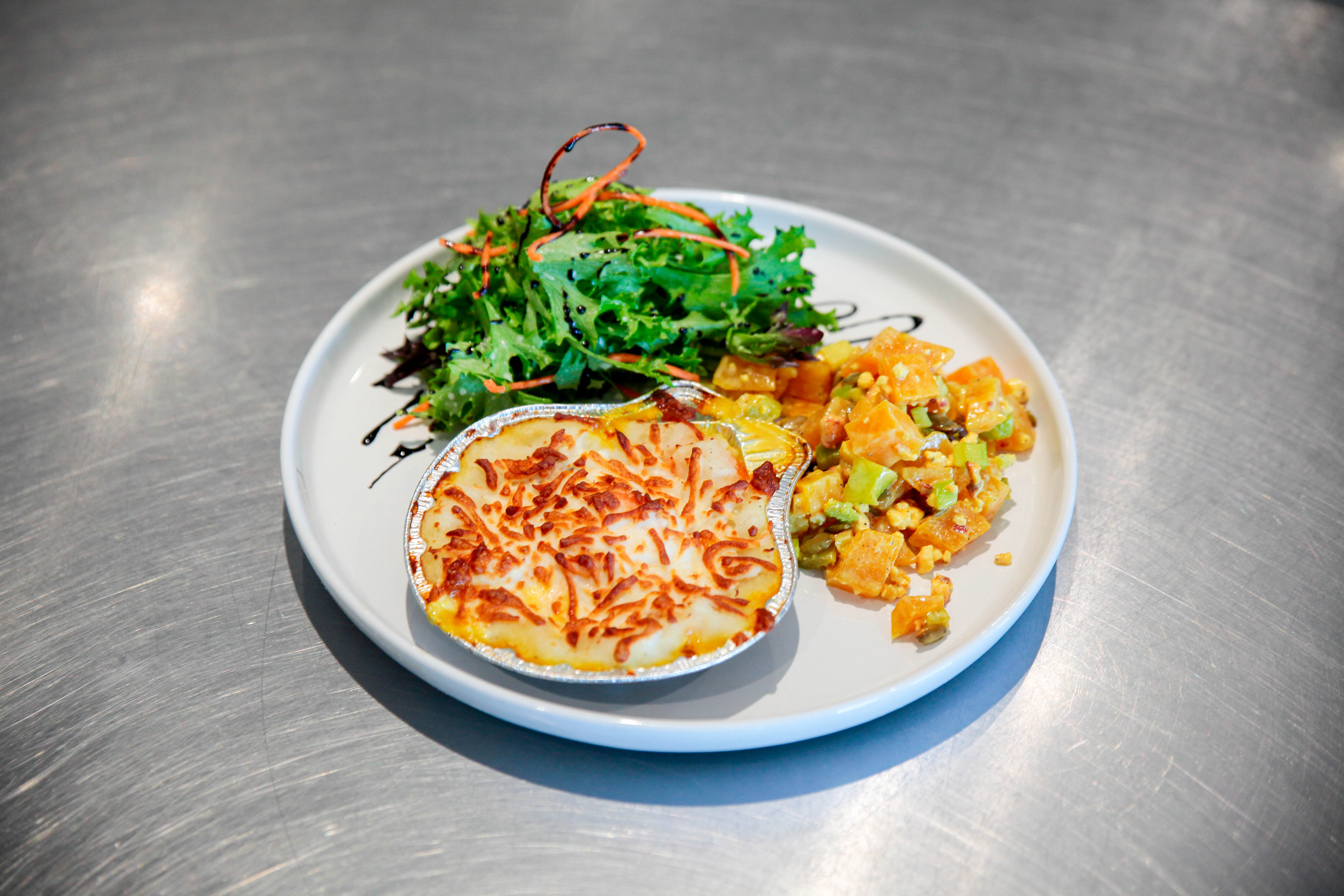 Here is the alt text for the image: "A white plate with a baked egg dish, a green salad and a side of vegetables on a stai...