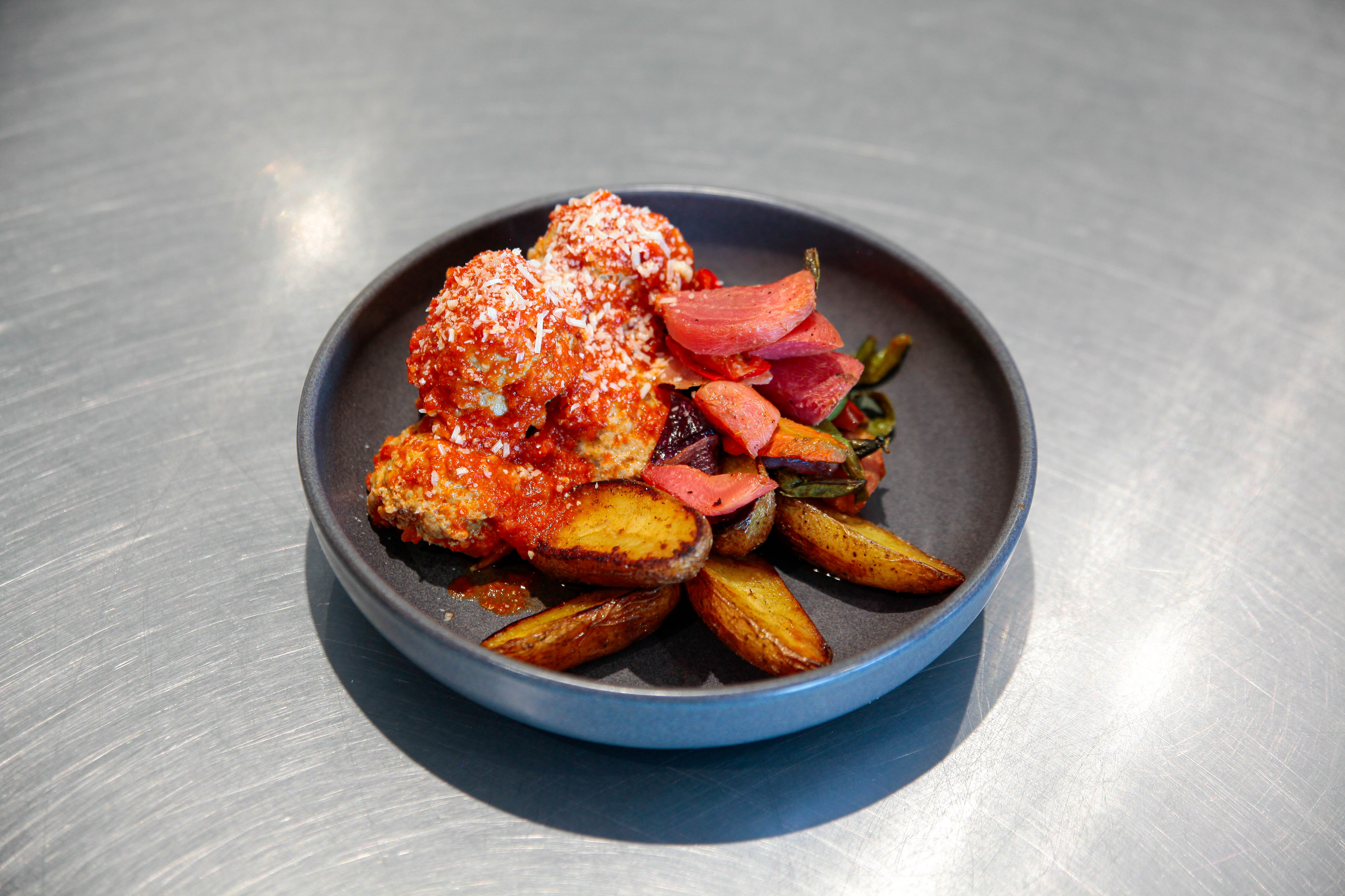 A plate of food sits on a metal surface. The plate is gray and contains a variety of dishes, including what appears to be ...