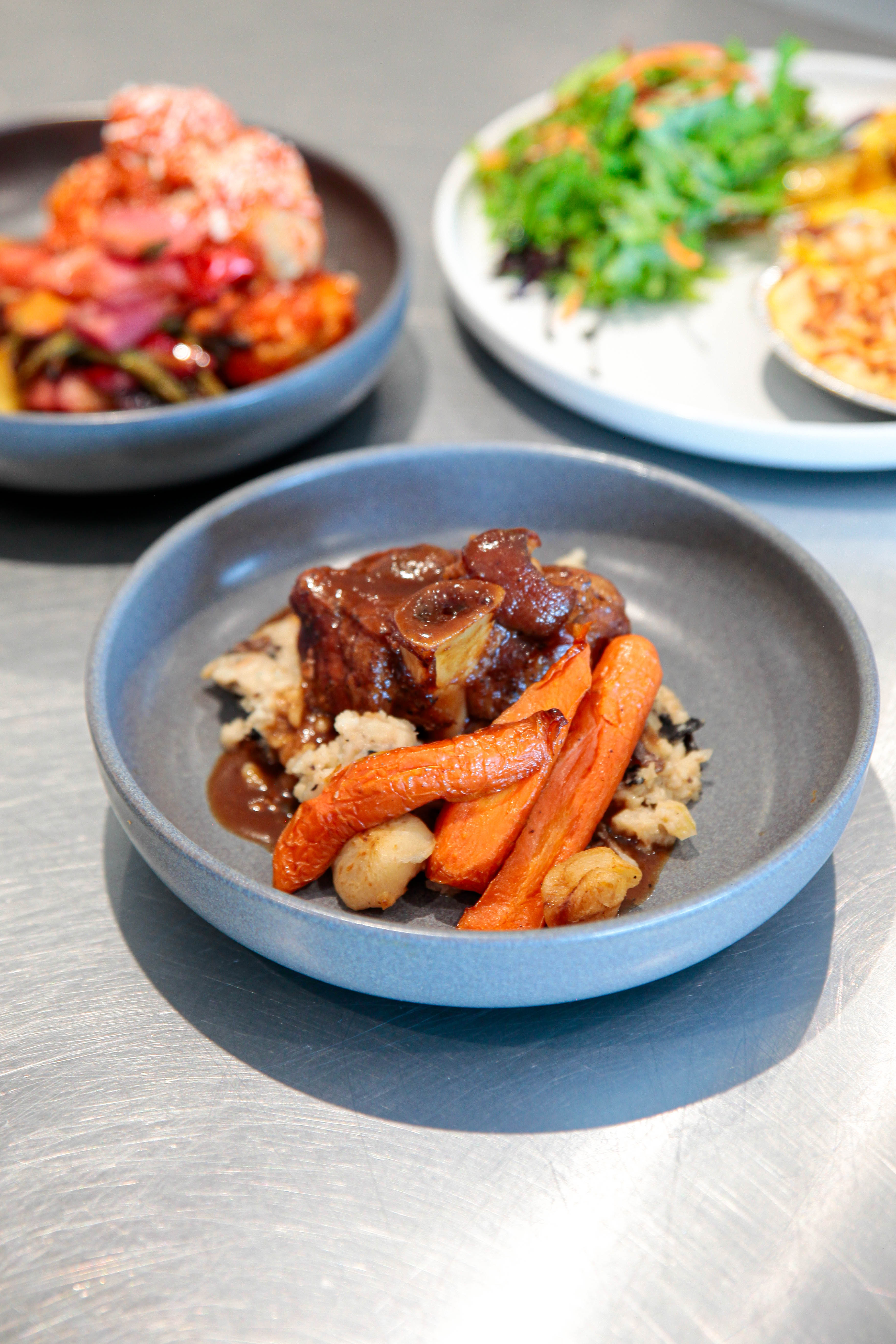 Présentation de plusieurs plats chauds des Toques Gourmandes alignés sur une table, mettant en valeur le menu à emporter.